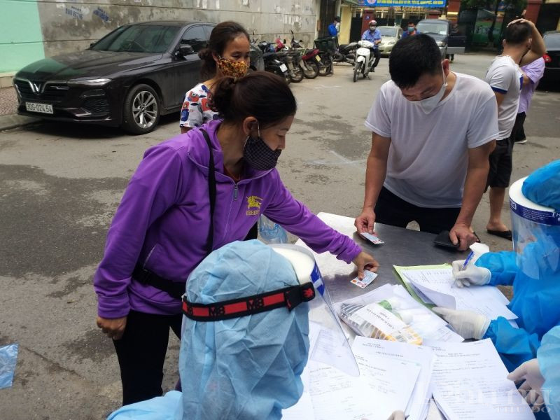 Tiểu thương chợ Ngã Tư Sở đến bàn đón tiếp, xuất trình giấy tờ để kiểm tra xem đúng đối tượng đã được sàng lọc và mời đến kiểm tra hay không Tiểu thương chợ Ngã Tư Sở đến bàn đón tiếp, xuất trình giấy tờ để kiểm tra xem đúng đối tượng đã được sàng lọc và mời đến kiểm tra hay không
