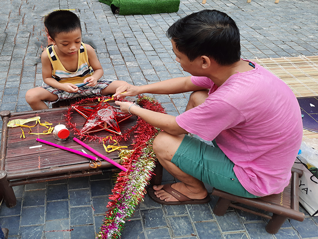 Bé Nguyễn Minh Phương, học sinh lớp 1A trường Tiểu học Văn Chương đang rất chăm chú cùng bố làm chiếc đèn ông sao của mình