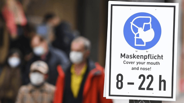 Một tấm biển có dòng chữ 'Cần đeo khẩu trang. Che miệng và mũi của bạn từ 8 - 22 giờ được gắn vào cột trên con đường trong một trung tâm mua sắm ở Frankfurt, Đức.