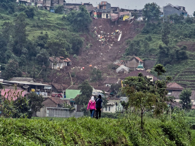 Người dân đi ngang qua địa điểm nơi một ngôi làng bị sạt lở đất vùi lấp.