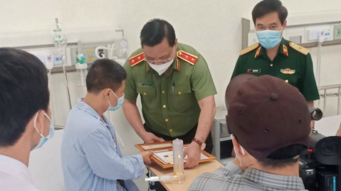 Trung tướng Nguyễn Hải Trung, Gi&aacute;m đốc C&ocirc;ng an th&agrave;nh phố H&agrave; Nội trao thư khen của Chủ tịch UBND th&agrave;nh phố v&agrave; giấy khen của Gi&aacute;m đốc C&ocirc;ng an th&agrave;nh phố cho anh Nguyễn Trần Minh tại Bệnh viện Qu&acirc;n y 103
