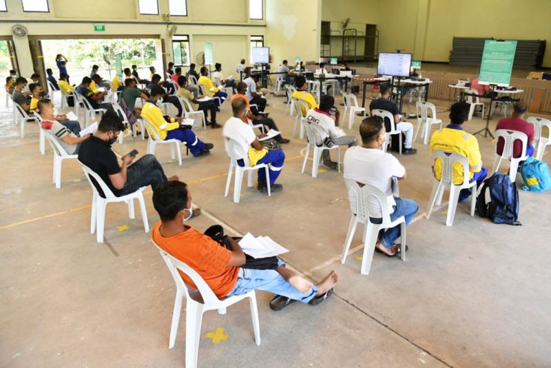 Công nhân nhập cư ngồi chờ tại khu vực theo dõi sau khi tiêm vắc-xin Covid-19 tại Trung tâm tiêm chủng Seletar, Singapore