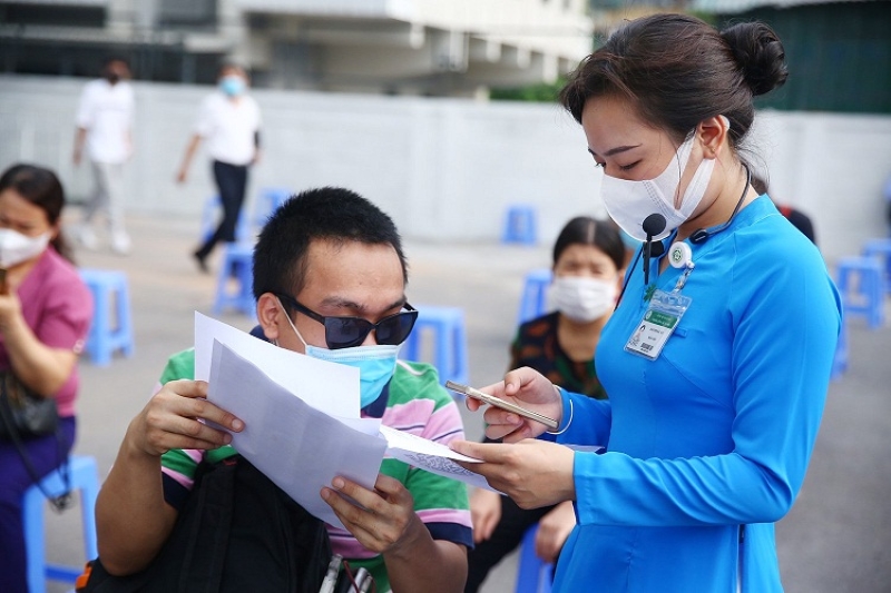 Người đến tiêm được hướng dẫn viên (áo dài xanh) hỗ trợ khai báo y tế và hoàn thiện thủ tục giấy tờ.