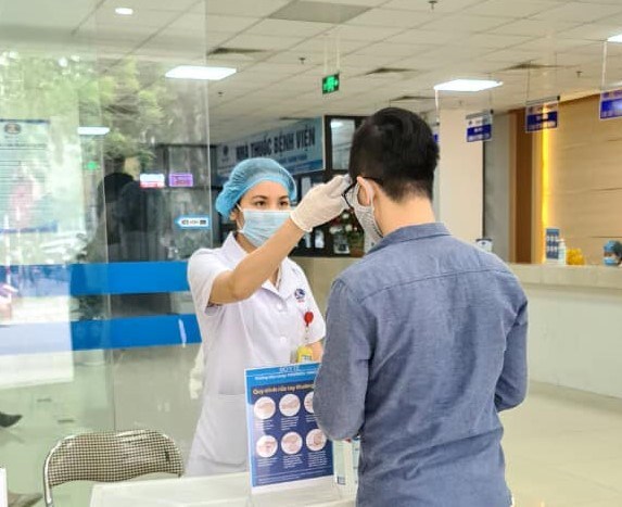 Bác sĩ  BV K Tân Triều kiểm tra nhiệt độ cho mọi người ra vào tại bệnh viện.