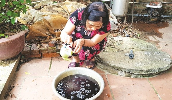 Bà Phan Thị Thanh Tùng ở khu dân cư Kim Anh, xã Thanh Xuân rót nước trà mạn vào chậu nước giếng khoan, nước nhanh chóng đổi màu tím đen.