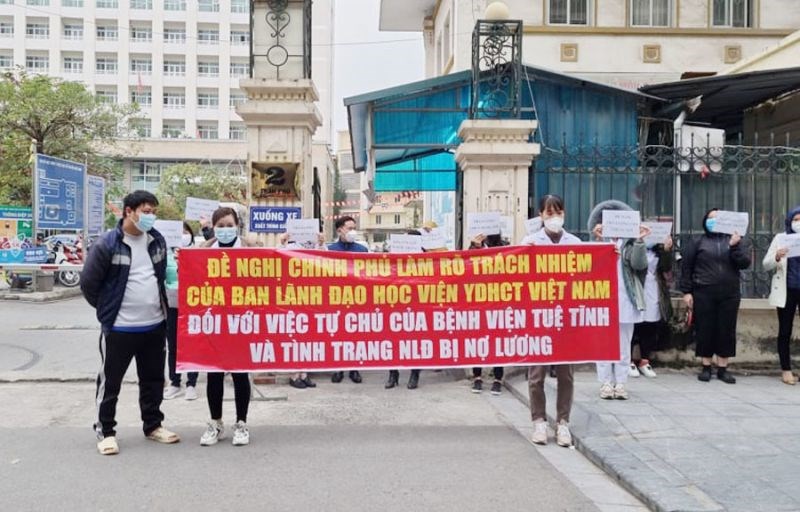 Hàng chục nhân viên y tế Bệnh viện Tuệ Tĩnh cầm băng rôn khẩu hiệu trước cổng Học viện Y dược học cổ truyền Việt Nam