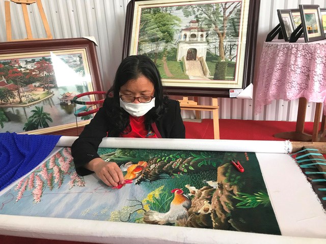 Nghệ nhân Hoàng Thị Khương bên bức tranh thêu phong cảnh - Ảnh: VGP/Diệu Anh
