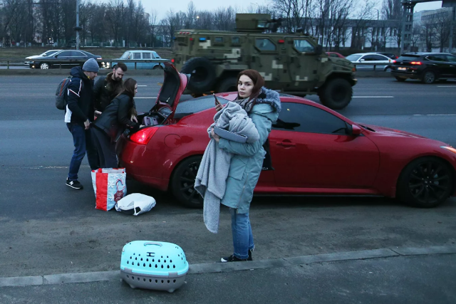 Người dân vội vã chất đồ đạc lên xe trên một trong những con phố ở Kiev, phía sau là xe quân sự.